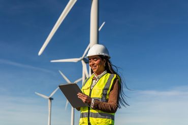 Woman engineer in safety gear using tablet near wind turbines.