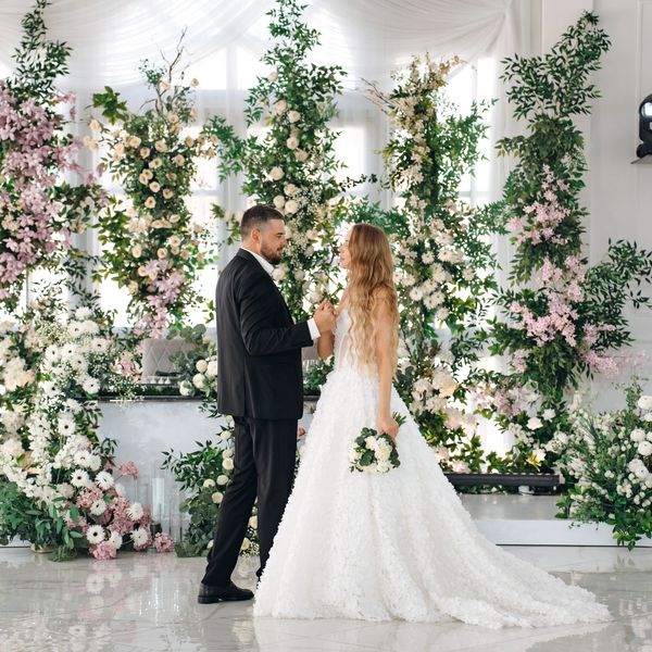 Bride and groom standing in front of a floral backdrop.