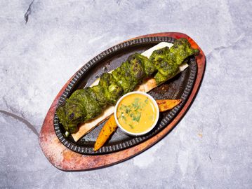 Grilled green marinated kebabs served with sauce and roasted potato wedges on a sizzling platter.