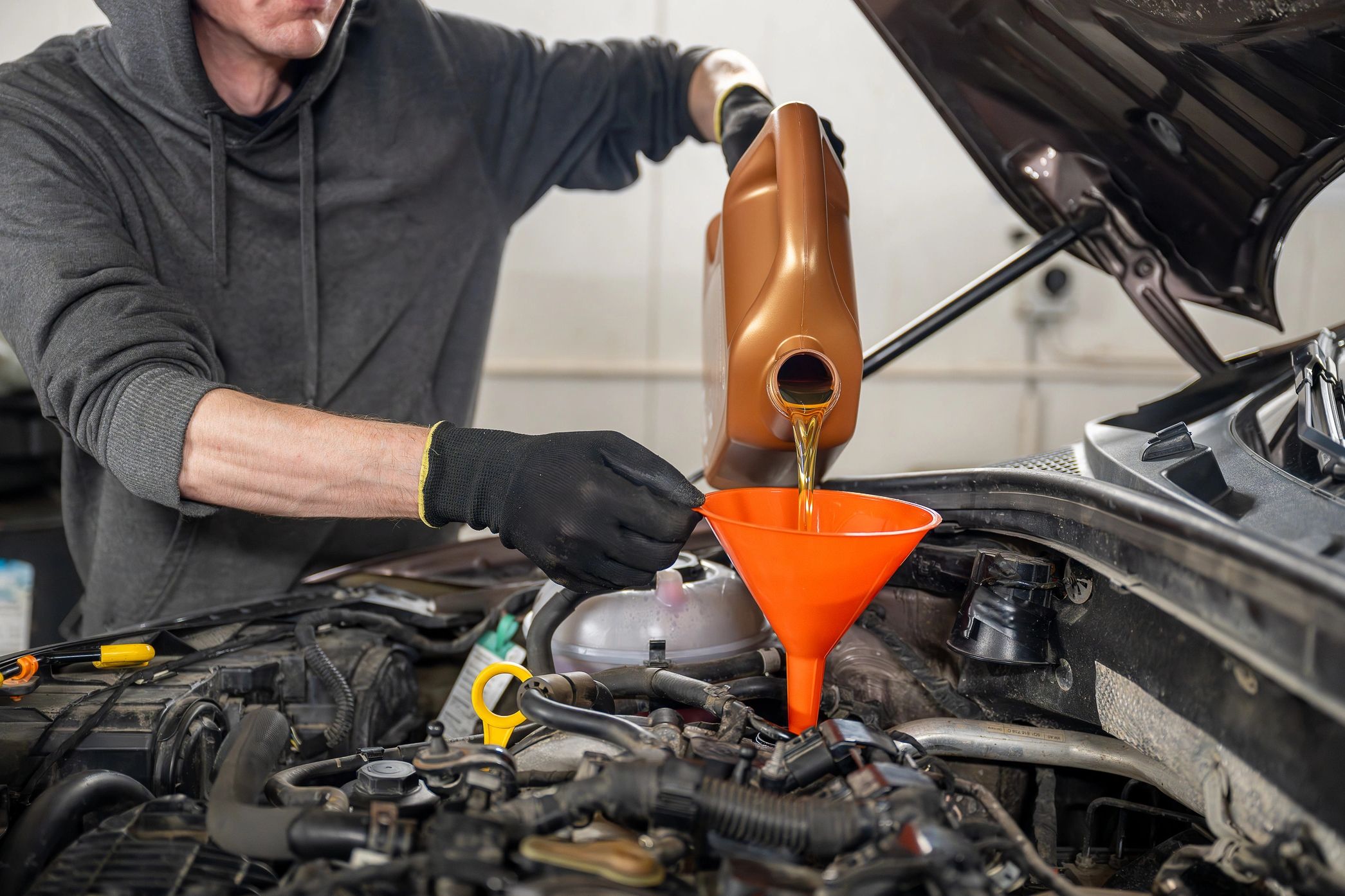 Man pouring motor oil into a car engine using a funnel.
