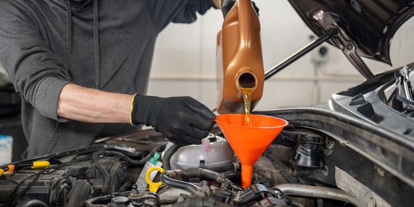 A person pouring engine oil into a car using a funnel.