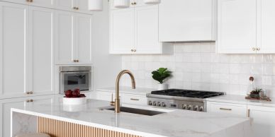 Modern white kitchen with gold faucet and marble island.