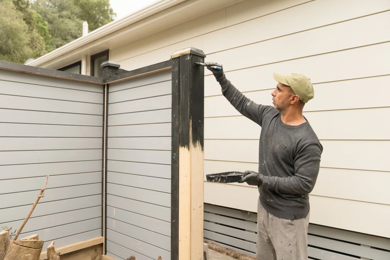 Man in gray shirt and a cap painting using paint brush outside residential home, home improvement concept.