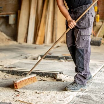 Person sweeping a dusty workshop floor.