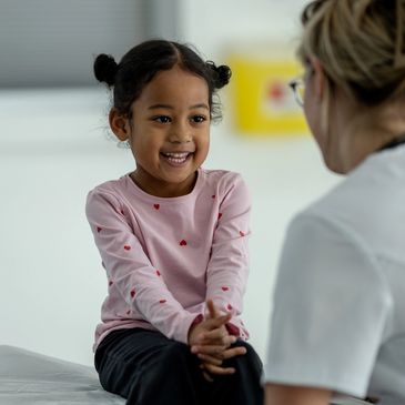 Smiling young girl talking to a healthcare professional in a bright room.