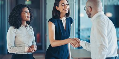 Two women and a man smiling and shaking hands in a professional setting.