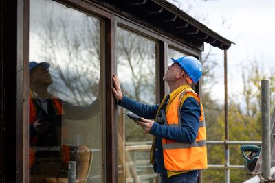 Construction worker inspecting a wooden window frame outdoors.
