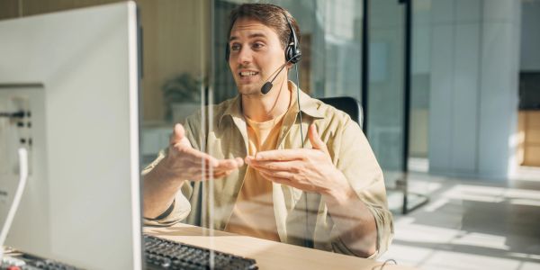 Man wearing headset talking and gesturing during a video call.