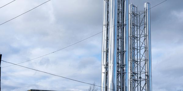 Tall shiny metal chimneys or towers against a cloudy sky.