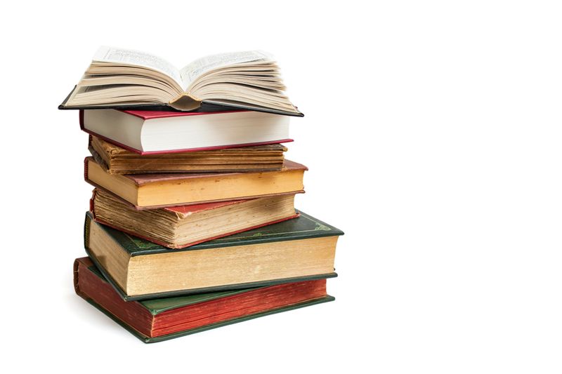 Vintage hard cover books stacked with an opened book on top, isolated on white background,