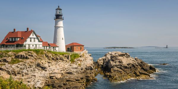 Lighthouse and house on rocky coastline under clear blue sky.
