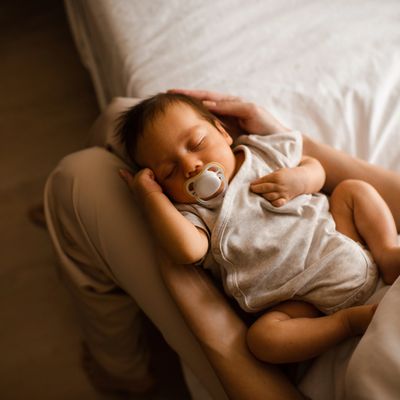 A newborn baby peacefully sleeping with a pacifier in someone's arms.