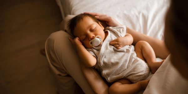 A baby peacefully sleeping with a pacifier in an adult's arms.