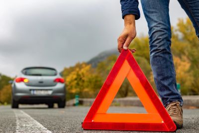Person placing a warning triangle on the road near a stopped car.