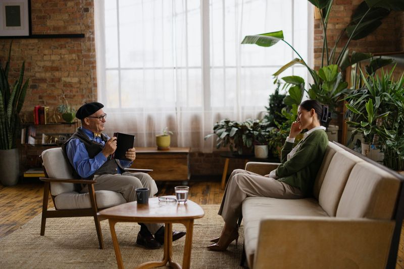 A professional therapist sits across from a patient, sharing a moment of connection, surrounded by plants in a cozy, natural-lit setting.