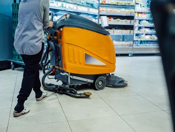 Person operating a floor cleaning machine in a store aisle.