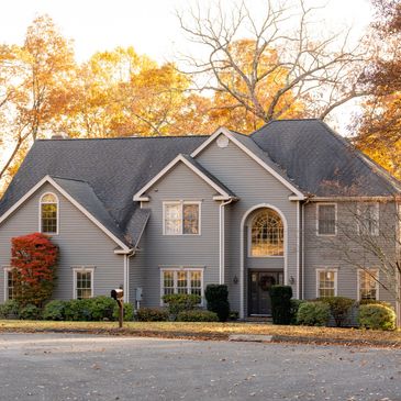 Large gray house surrounded by autumn trees with colorful leaves.