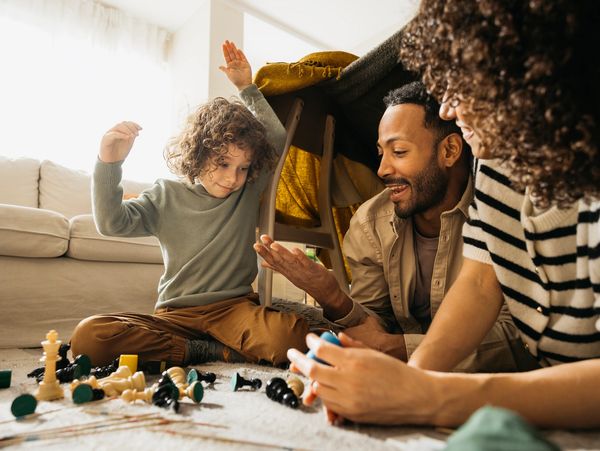Family joyfully playing chess on the floor with a cozy blanket fort.