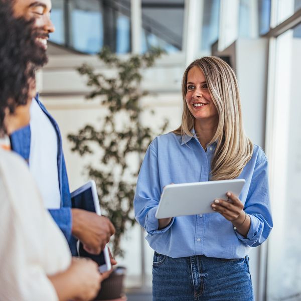 A woman holding a tablet engages in a lively discussion with colleagues in a modern office.