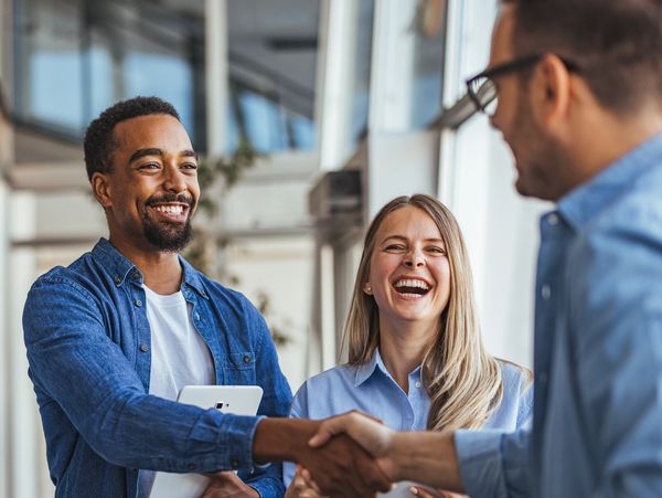 Three colleagues smiling, shaking hands, and sharing a positive moment at work.