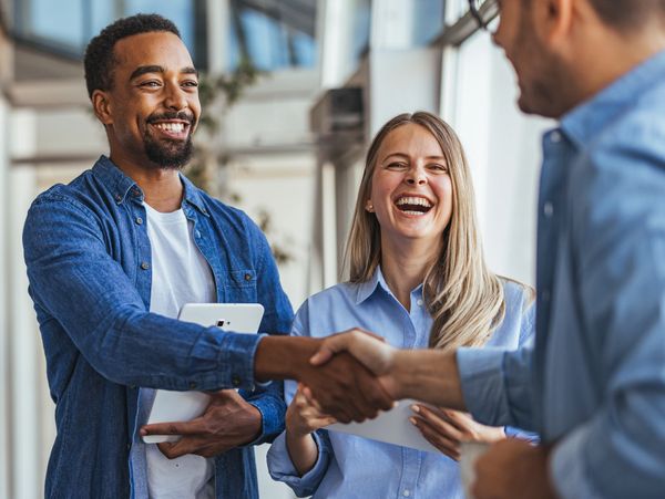 Three colleagues smiling and shaking hands in a bright office space.