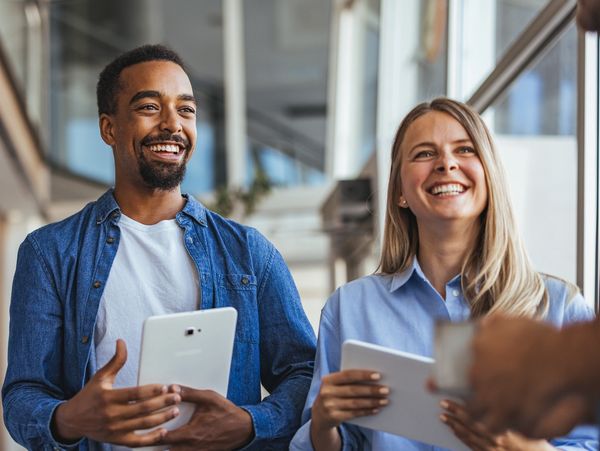 Two colleagues smiling and holding tablets during a casual meeting.