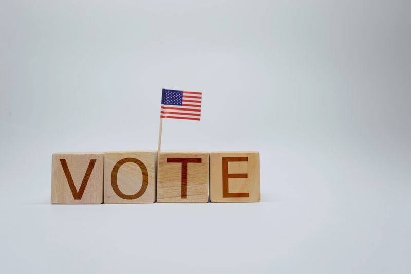 Wooden blocks spell out the word 'Vote,' complemented with a small American flag on a stick