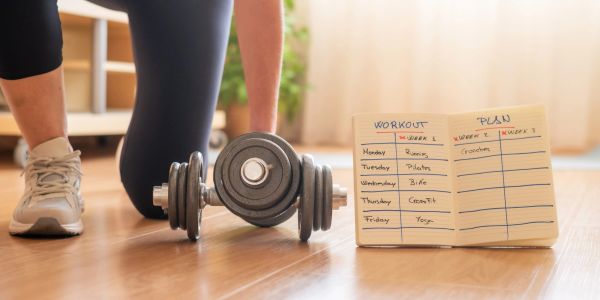 Workout plan, dumbbell, and person in workout shoes.