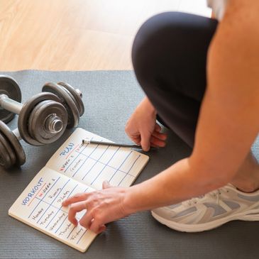 Person planning workout schedule with dumbbells nearby on a mat.