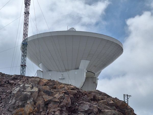 Large satellite dish on rocky hill under cloudy sky.
