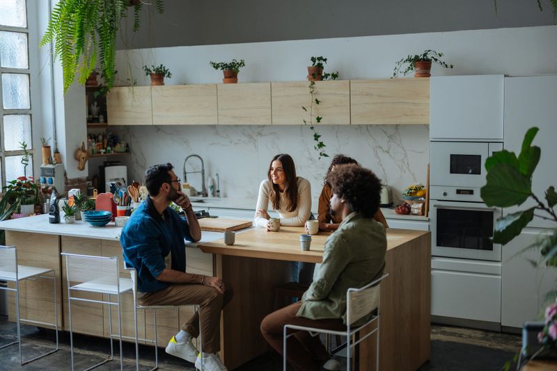 Four diverse friends enjoying a relaxing morning, sharing stories and sipping coffee in a stylish, plant-filled kitchen