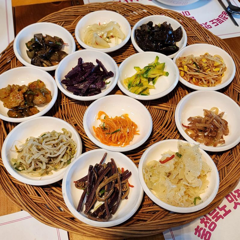An assortment of colorful banchan, featuring kimchi, seasoned vegetables, pickled radish, and marinated seaweed. These Korean side dishes bring a variety of textures and flavors to the table.