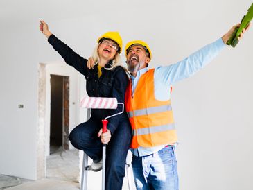Two construction workers joyfully celebrate inside a newly renovated space.