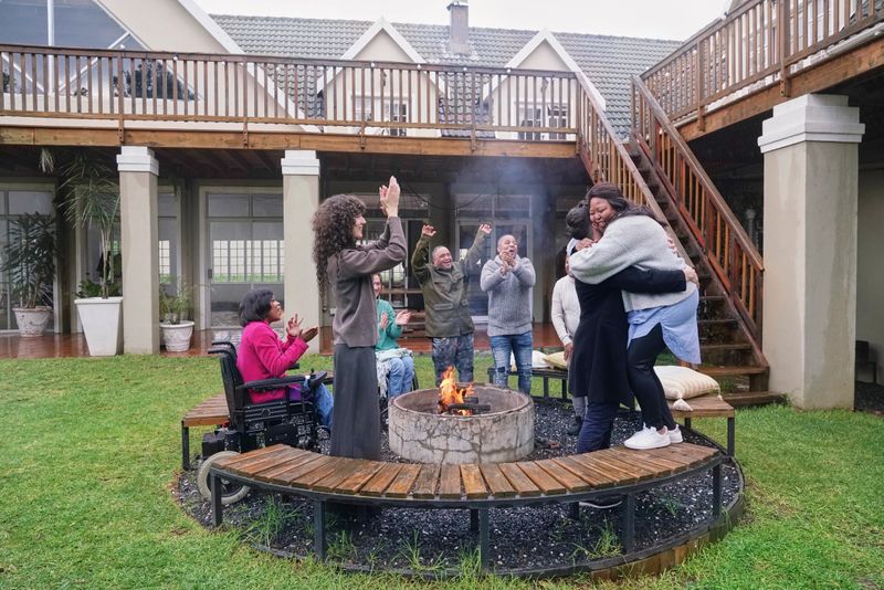 Friends with various disabilities cheering and clapping for lesbian couple embracing by fire pit in backyard