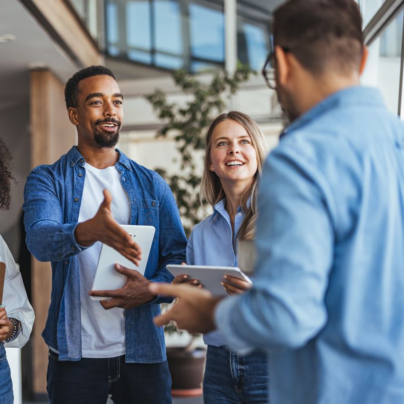 Diverse group of professional colleagues engaged in a lively business meeting, exchanging ideas and smiles, illustrating teamwork, collaboration, and a dynamic office environment.