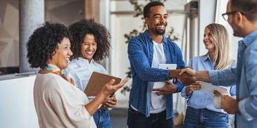 Happy colleagues shaking hands and laughing in a modern office.