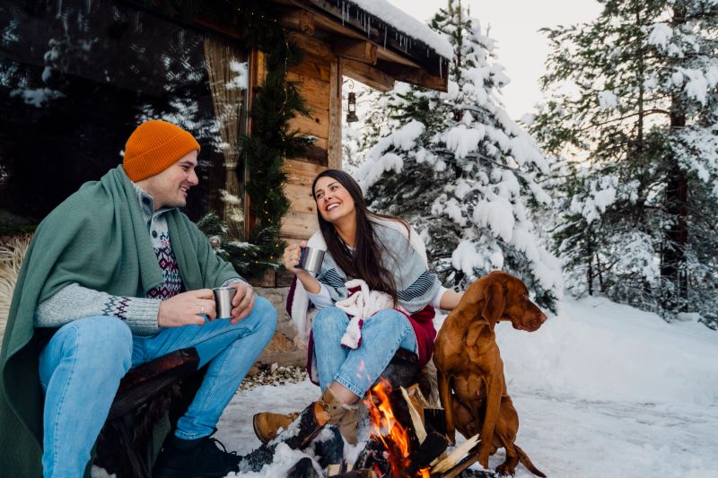 Couple with dog siting around fire pit in front of the cabin