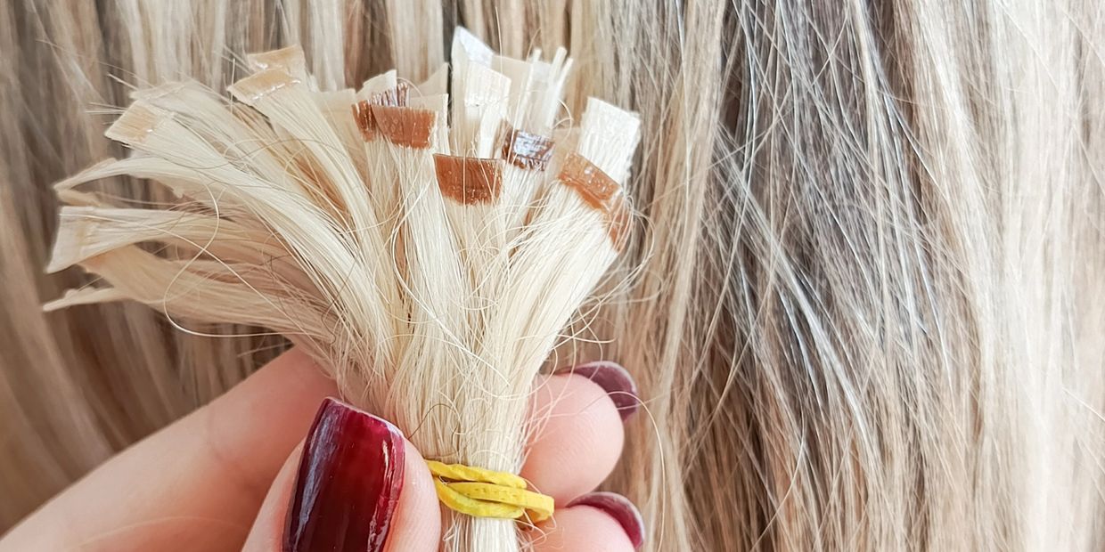 Close-up of blonde hair extensions held by a hand with dark red nails.
