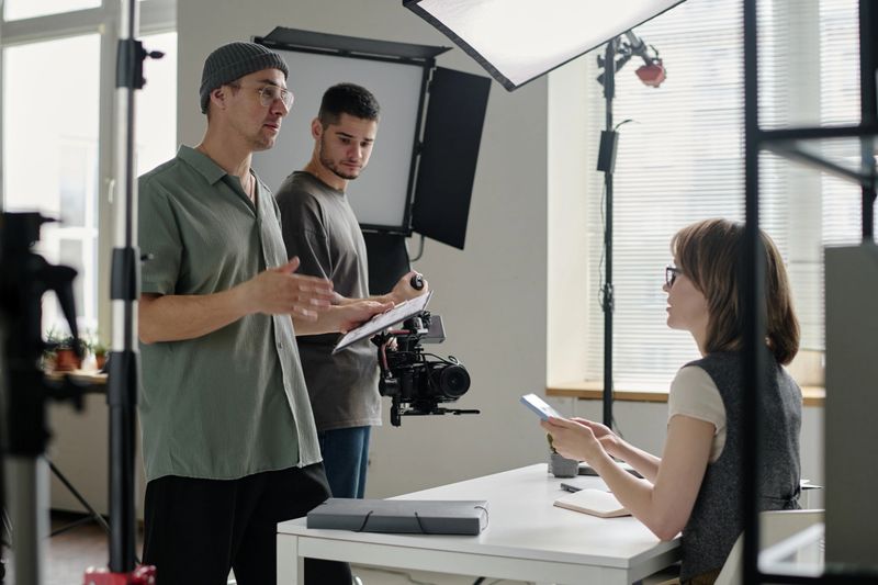 Male talented director discussing shooting day with crew, actress looking at him and listening his speech while cameraman setting device