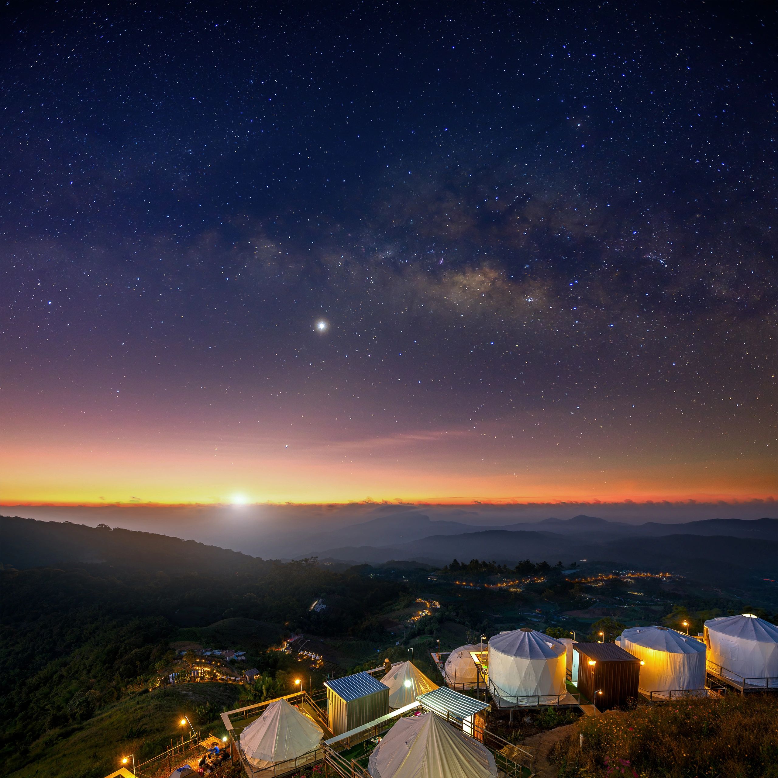 Starry night sky over a scenic campsite at sunset.
