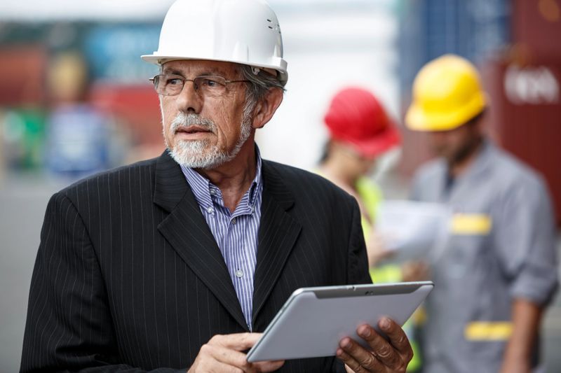 Portrait of a foreman standing confidently at the dock, wearing a white hard hat and using digital tablet to oversee shipping operations at a warehouse, inspecting containers, managing logistics and inventory control