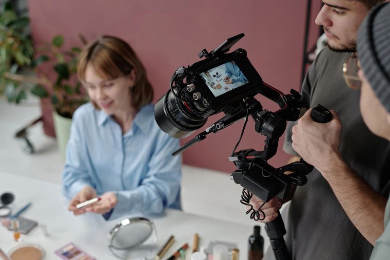 High angle shot of director and operator looking at camera display while shooting commerce with woman demonstrating cosmetic products