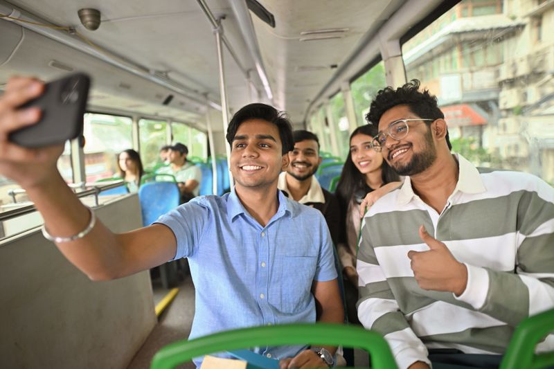 A young boy captures a selfie of his group of friends while they engage in lively conversation on a bus. The cheerful expressions and casual setting highlight a fun and memorable moment of connection during their journey, reflecting the joy of shared experiences.