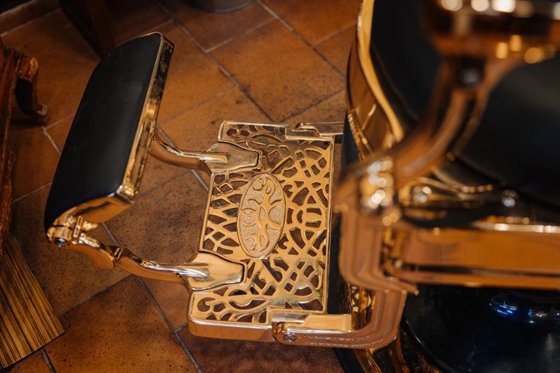 A barber chair with a gold foot rest. The chair is in a room with a brown floor