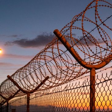 High‑security fence with coiled barbed wire at sunset, symbolising justice and perimeter control.
