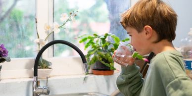 Young boy drinking water from a glass in the kitchen near the sink.