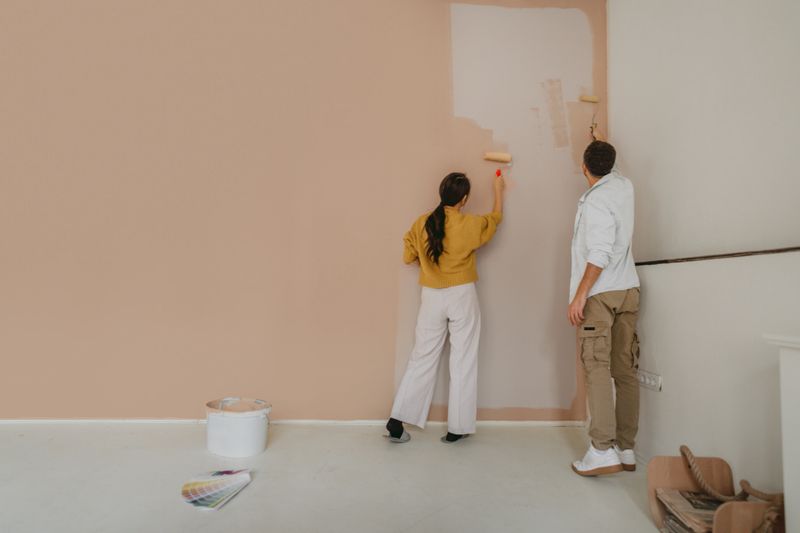 Photo of a couple joyfully transforming their living space by painting a wall together, creating a beautiful and inviting atmosphere during their home renovation