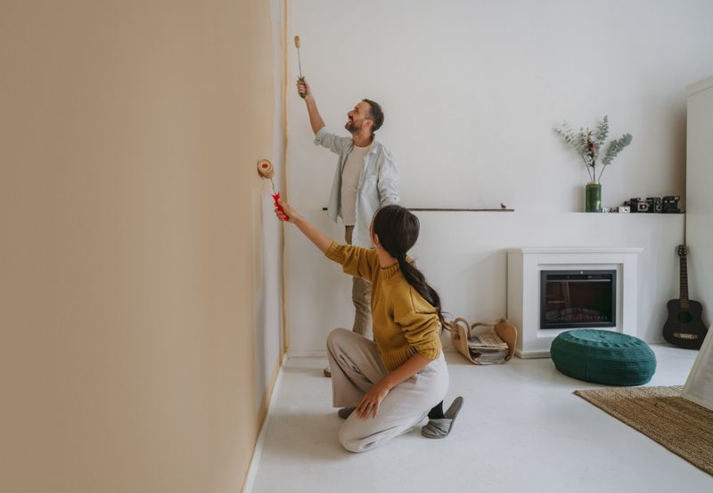 Photo of a couple joyfully transforming their living space by painting a wall together, creating a beautiful and inviting atmosphere during their home renovation