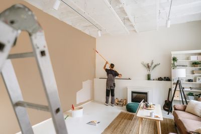 Person painting a wall beige in a bright living room.