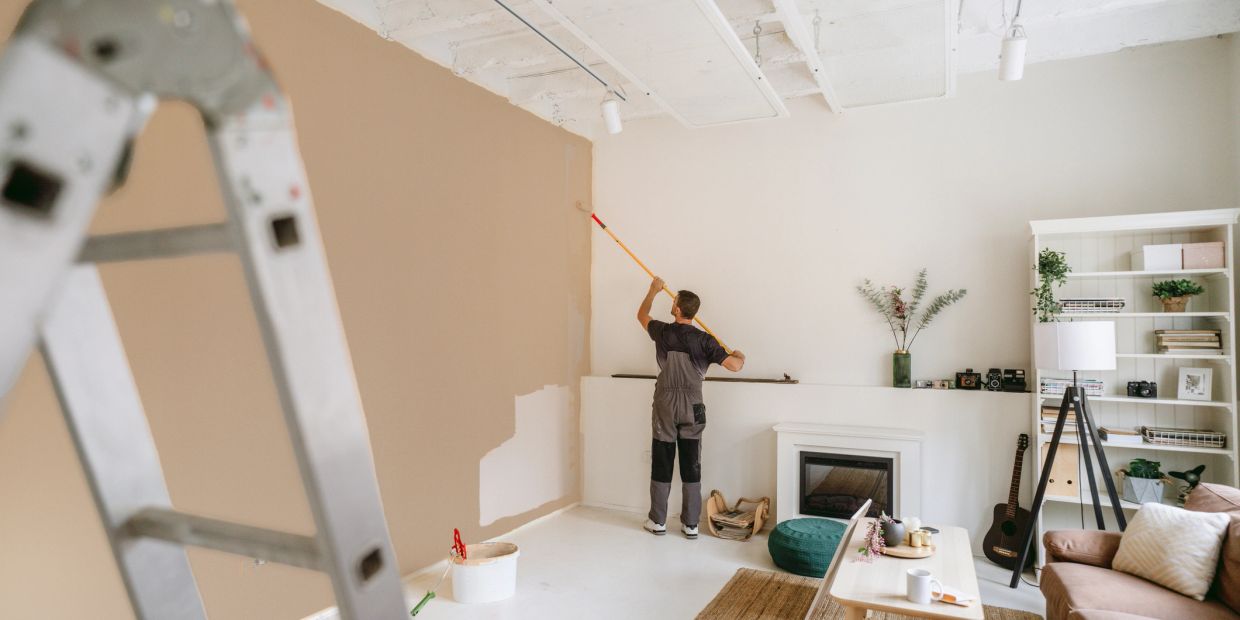 Man painting wall beige in a living room.